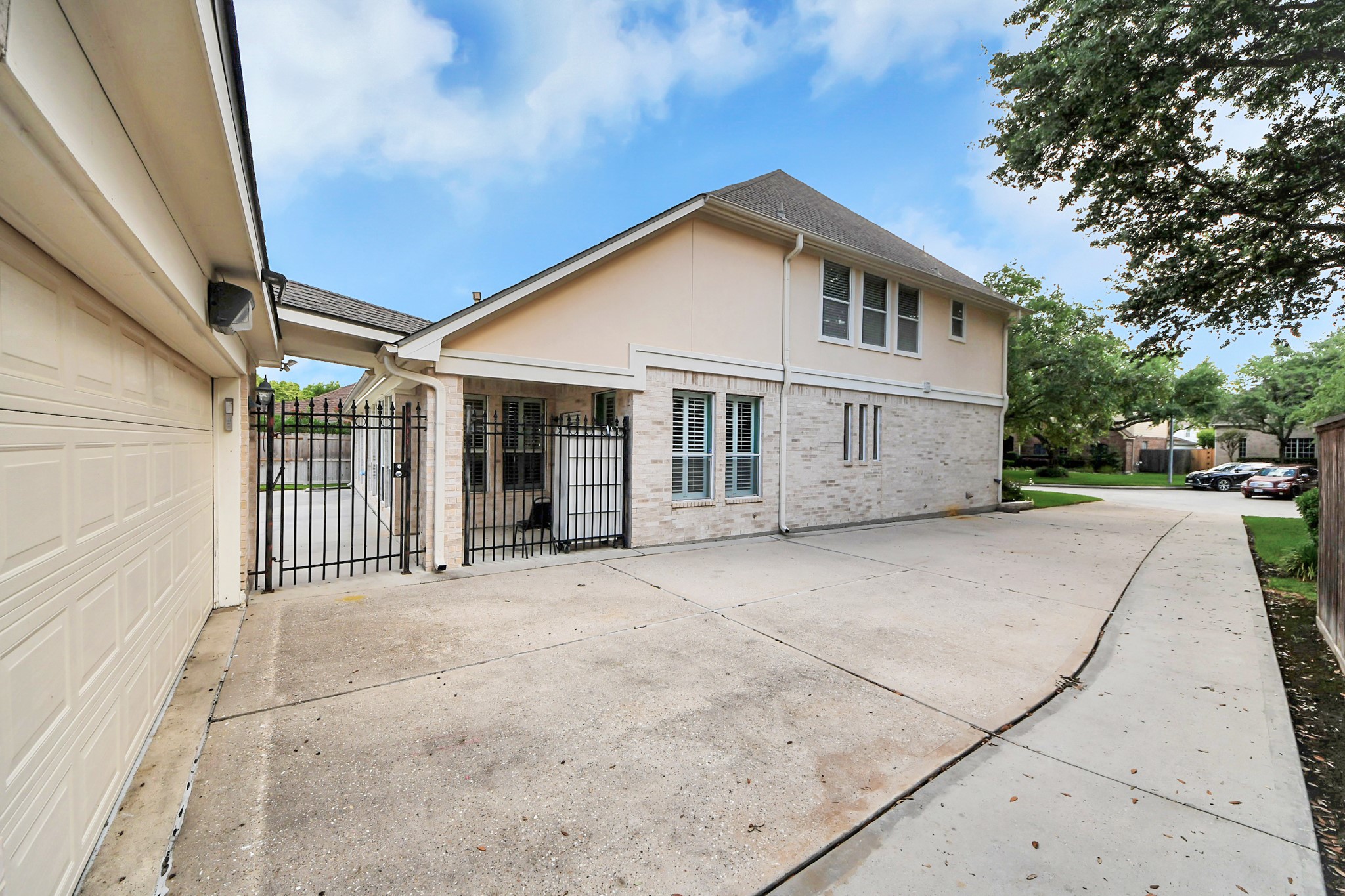 20111 Biscayne Hill Court Spring, TX 77379 - Photo 36 of 44 This photo showcases a modern two-story home with a light brick exterior and a pitched roof. It features a spacious driveway leading to a secure gated area and a two-car garage. The surrounding area is landscaped with mature trees, providing a welcoming neighborhood feel.