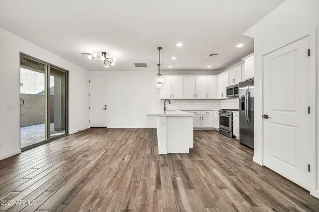 a view of an empty room with wooden floor and a kitchen
