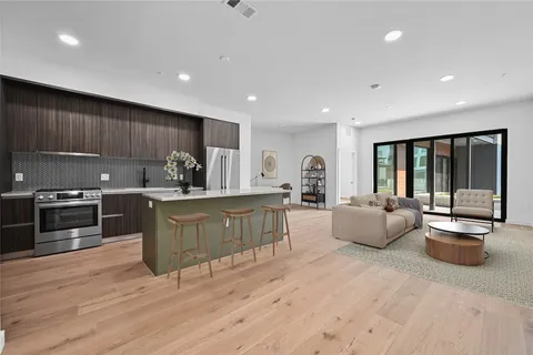 a kitchen with stainless steel appliances granite countertop a stove a sink a refrigerator and couches with wooden floor