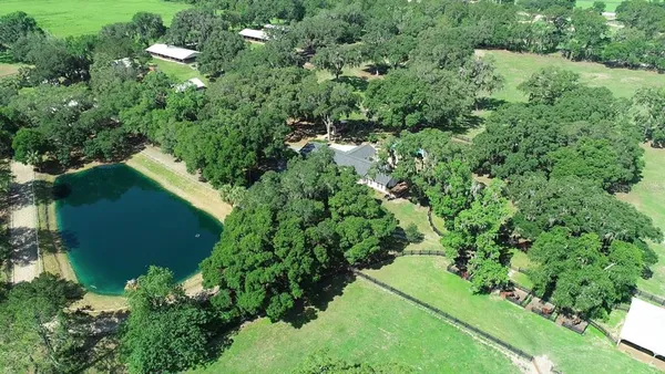an aerial view of residential house with outdoor space and trees all around