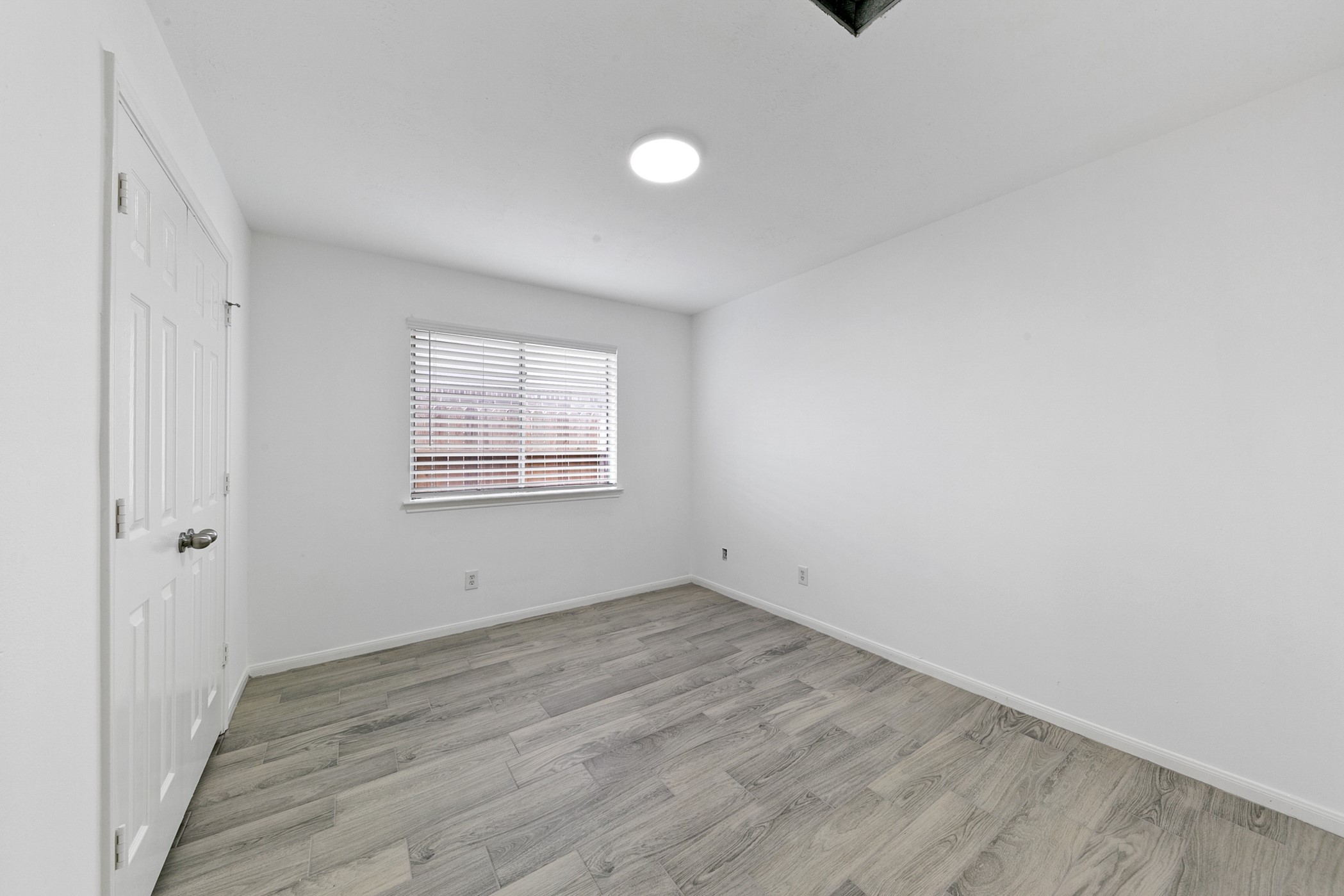 12014 Raven View Drive Houston, TX 77067 - Photo 10 of 29 This room features a clean, modern design with white walls and wood-look flooring. A window with blinds allows natural light, and there's a door on the left side. Ideal for a bedroom or office space.