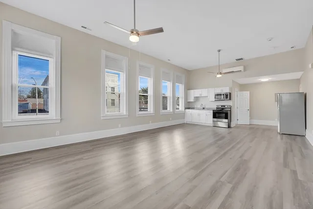a view of an empty room with wooden floor kitchen view and a window