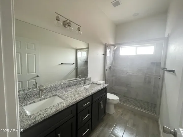 a bathroom with a granite countertop sink a toilet a mirror and shower
