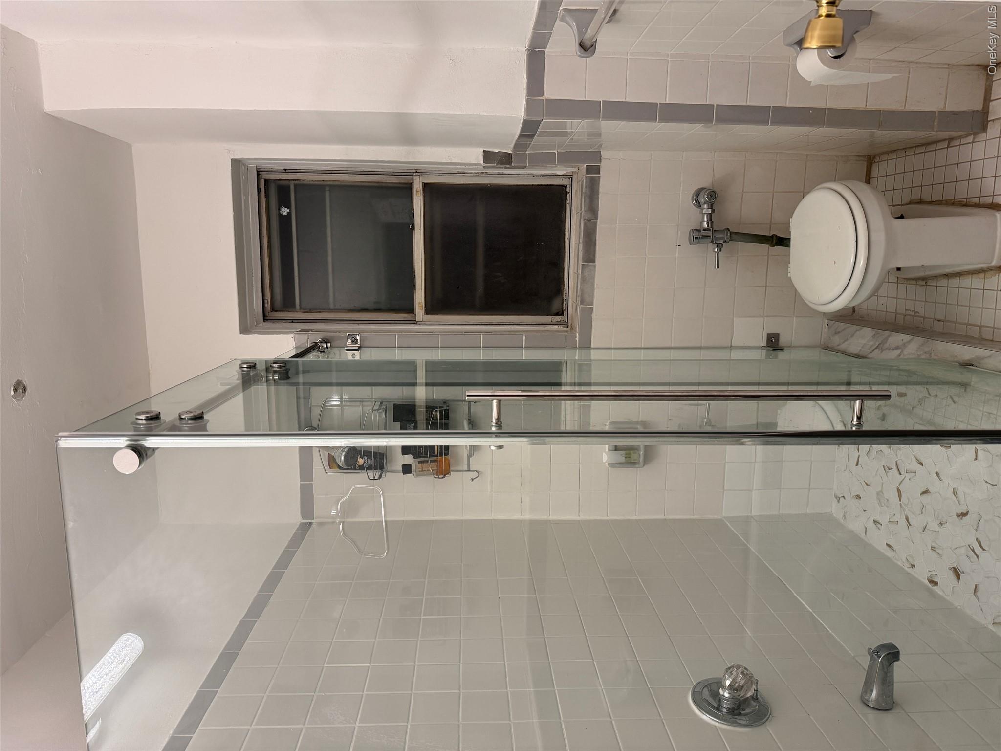 141-17 78th Road, Unit 1O Queens, NY 11367 - Photo 10 of 17 Full bathroom featuring tile walls, light tile patterned floors, a stall shower, and wainscoting