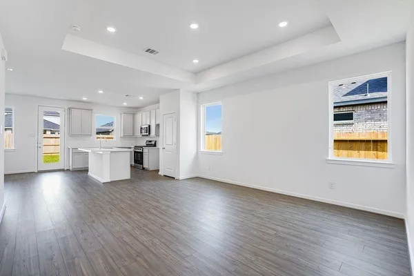 a view of an empty room and kitchen with wooden floor