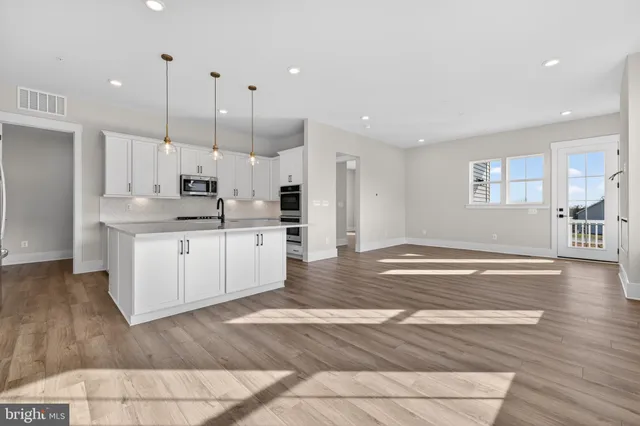 a large kitchen with stainless steel appliances kitchen island granite countertop a stove a sink a refrigerator and white cabinets with wooden floor