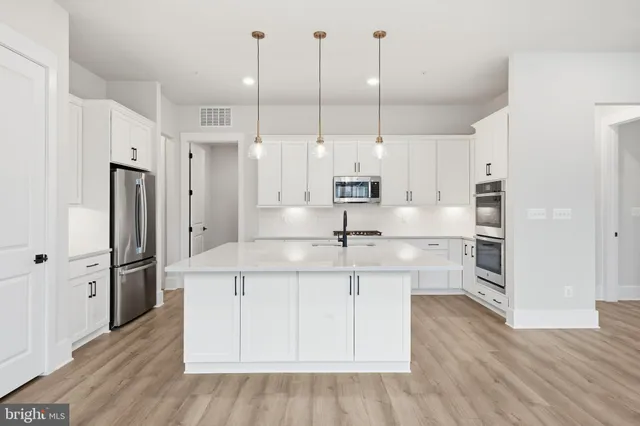 a open kitchen with stainless steel appliances kitchen island granite countertop a refrigerator a sink and white cabinets with wooden floor