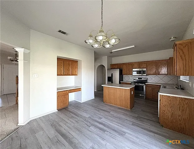 a kitchen with stainless steel appliances granite countertop a refrigerator a stove oven a sink dishwasher and white cabinets with wooden floor