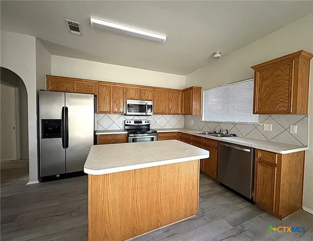 a kitchen with stainless steel appliances granite countertop a sink a stove a refrigerator with grey cabinets and wooden floor