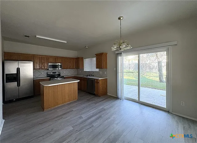 a kitchen with stainless steel appliances granite countertop a refrigerator a sink dishwasher a stove and a large countertops with wooden floor