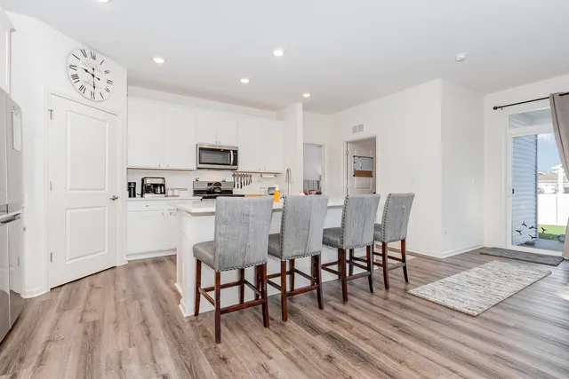 a living room with stainless steel appliances furniture wooden floor and a kitchen view