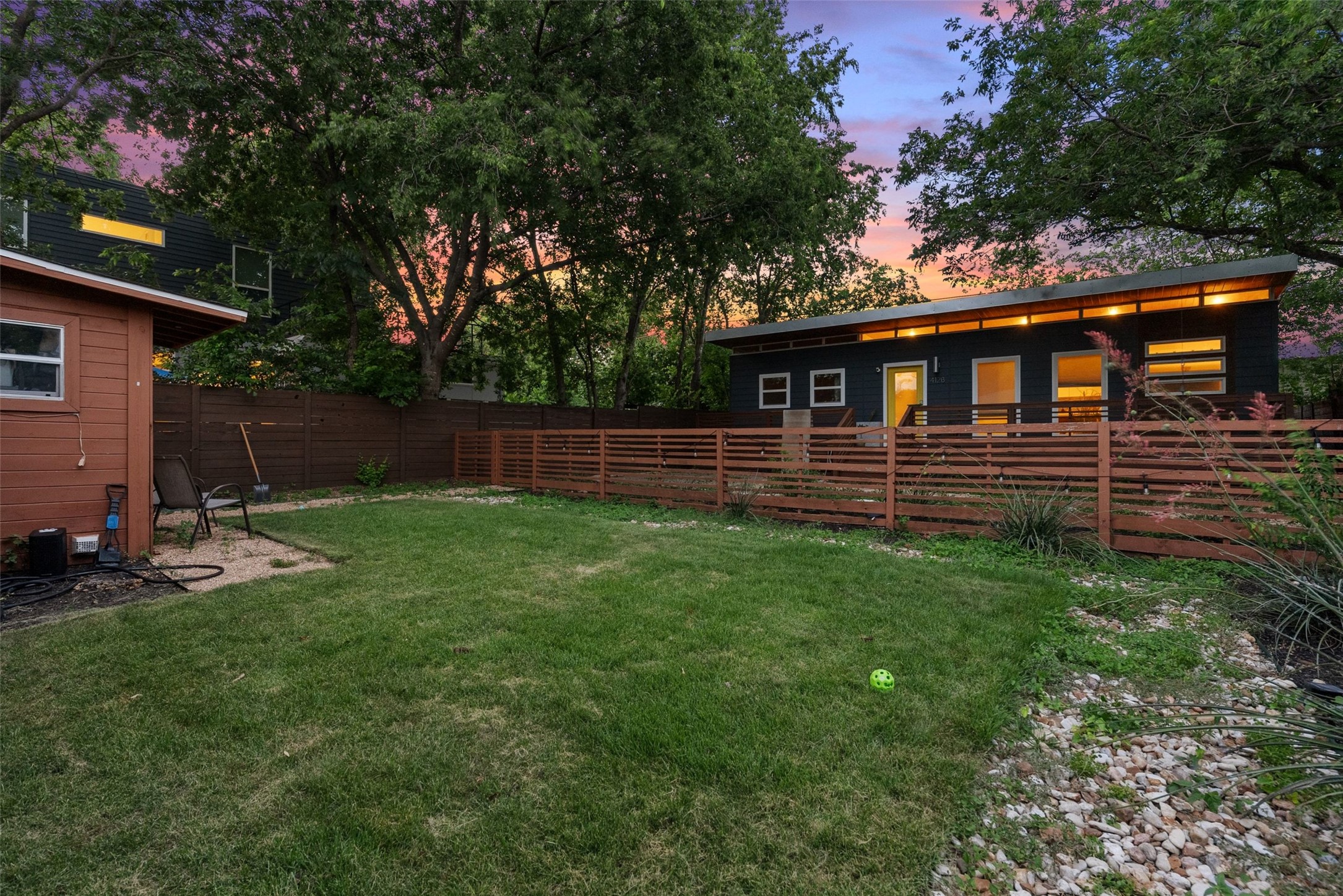 412 West Croslin Street Austin, TX 78752 - Photo 20 of 36 A spacious yard with mature trees backs to a modern structure, fully fenced for privacy.