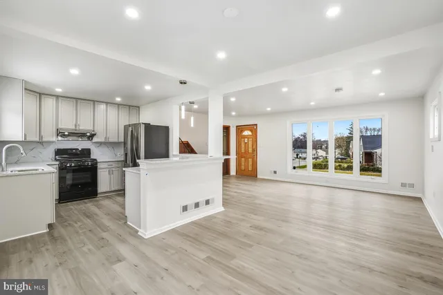 a large white kitchen with stainless steel appliances granite countertop a large counter top a stove and a refrigerator with wooden floor