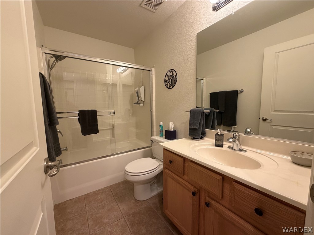2416 North Ridge Avenue Bullhead City, AZ 86429 - Photo 16 of 33 Full bathroom featuring vanity, combined bath / shower with glass door, dark tile patterned flooring, and a textured wall