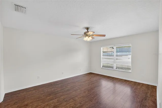 a view of an empty room with wooden floor and a ceiling fan