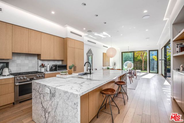 a kitchen with stainless steel appliances granite countertop a stove top oven a sink dishwasher a dining table and chairs with wooden floor