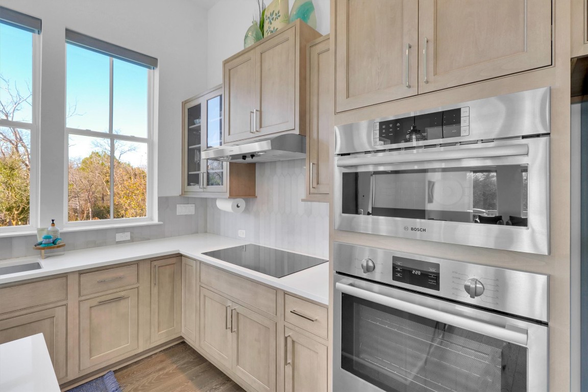 4806 Olive Sparrow Drive, Unit C Austin, TX 78723 - Photo 12 of 32 Kitchen with light brown cabinetry, under cabinet range hood, black electric stovetop, light wood-style floors, and decorative backsplash