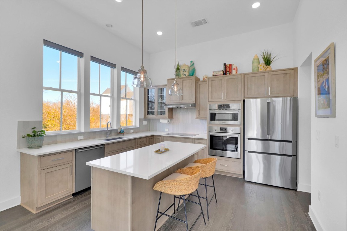 4806 Olive Sparrow Drive, Unit C Austin, TX 78723 - Photo 10 of 32 Kitchen with appliances with stainless steel finishes, light brown cabinetry, glass insert cabinets, decorative light fixtures, and a kitchen bar