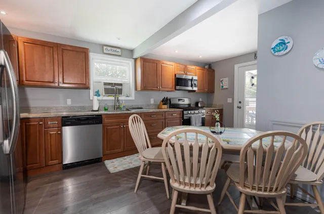 a kitchen with stainless steel appliances granite countertop a table chairs a sink dishwasher a microwave oven and a refrigerator with wooden floor