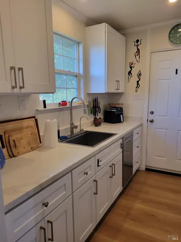 a kitchen with a sink dishwasher and white cabinets with wooden floor