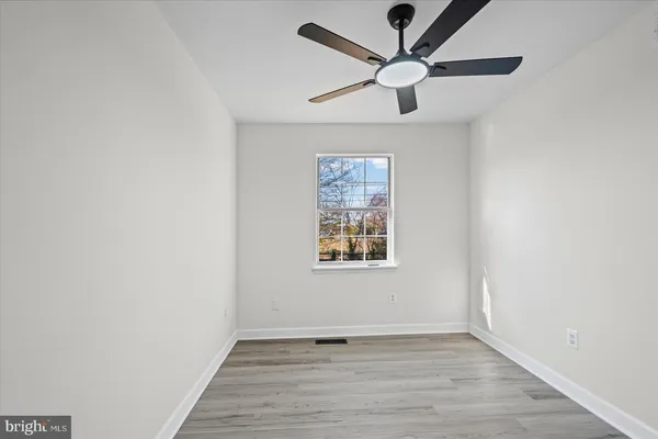 an empty room with wooden floor ceiling fan and windows