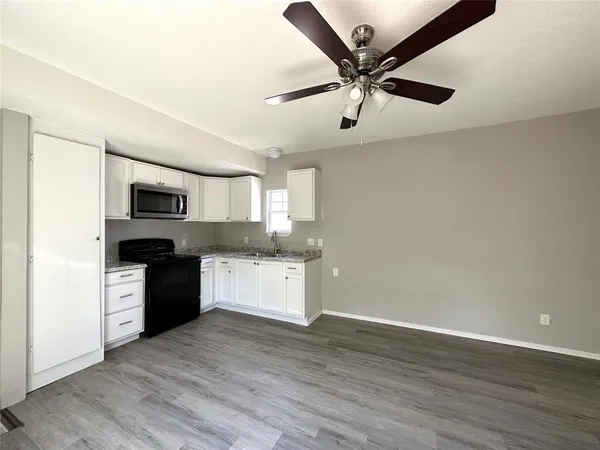 a kitchen with stainless steel appliances granite countertop a refrigerator a sink a stove and white cabinets with wooden floor