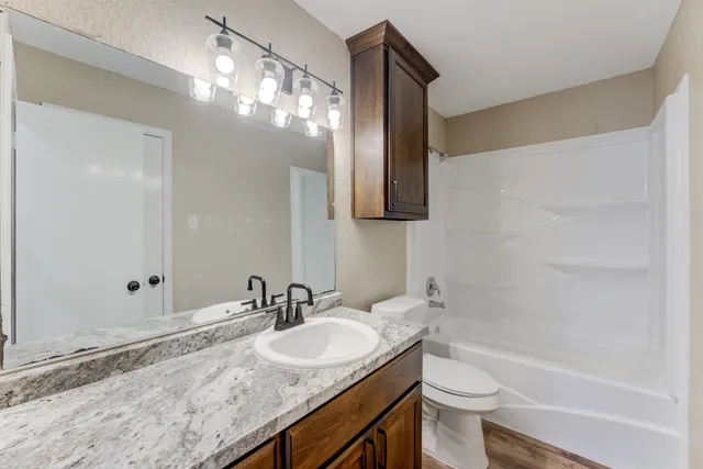 a bathroom with a granite countertop sink a toilet and shower