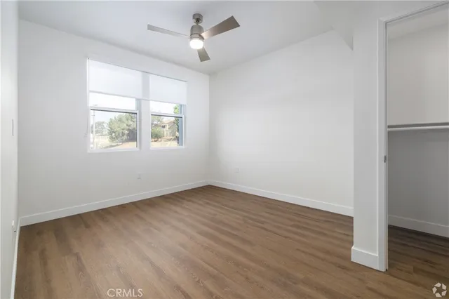 an empty room with wooden floor ceiling fan and windows