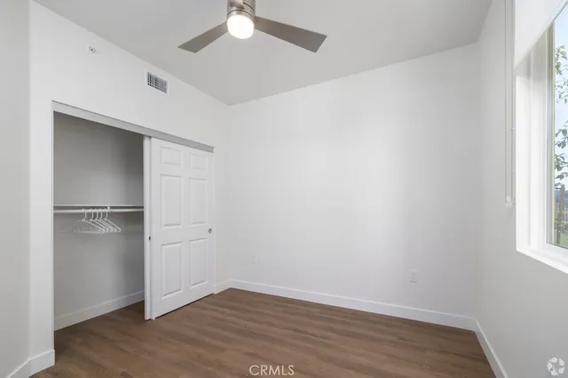 an empty room with wooden floor closet and windows