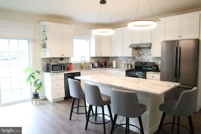 a kitchen with granite countertop a refrigerator a stove a sink dishwasher a dining table and chairs with wooden floor