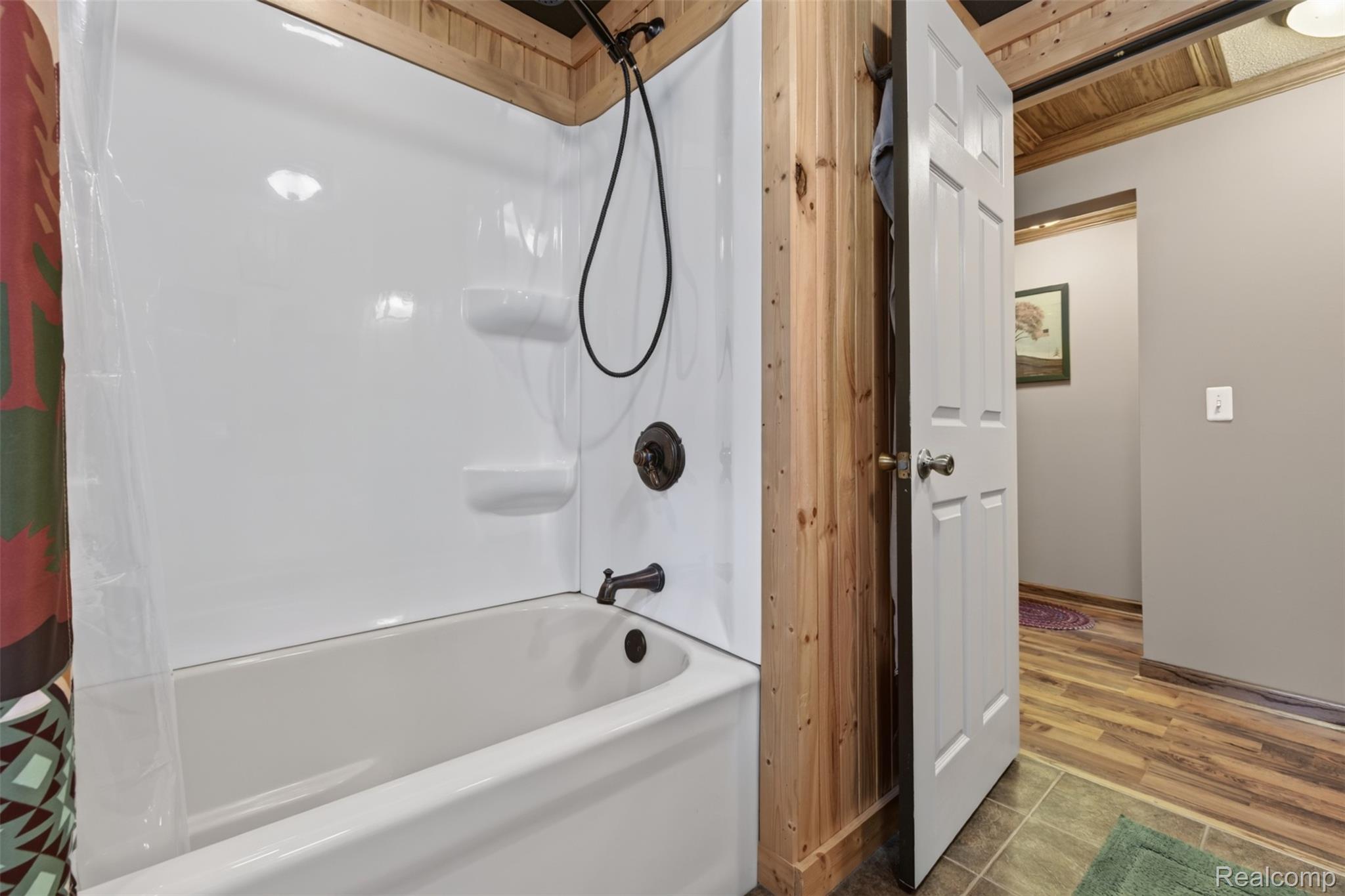 5977 Anglers Road Ortonville, MI 48462 - Photo 24 of 63 White bathtub with shower, bronze fixtures, natural wood-paneled walls, and wood-finish flooring