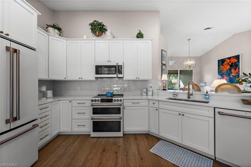 9331 Spring Run Boulevard, Unit 3005 Estero, FL 34135 - Photo 2 of 48 White shaker cabinetry with gold-toned hardware, wood-finish flooring, white subway tile backsplash, and stainless steel appliances