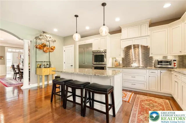 a kitchen with stainless steel appliances granite countertop a stove top oven a refrigerator a sink and white cabinets with wooden floor