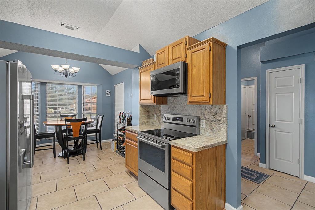 645 Cross Ridge Circle Fort Worth, TX 76120 - Photo 9 of 26 Kitchen featuring stainless steel appliances, light tile patterned floors, tasteful backsplash, a chandelier, and wood finish cabinets