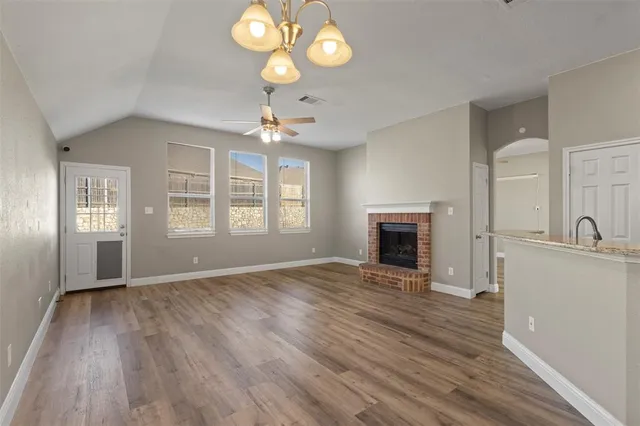 an empty room with wooden floor fireplace and windows
