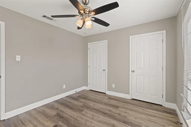 an empty room with wooden floor fan and windows