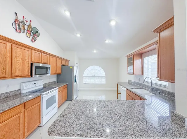 a large kitchen with stainless steel appliances kitchen island granite countertop a refrigerator and a sink