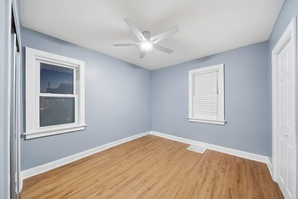 an empty room with wooden floor closet and windows