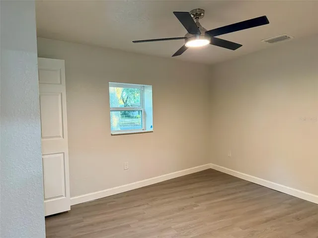 an empty room with wooden floor fan and windows