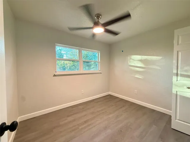 an empty room with wooden floor fan and windows