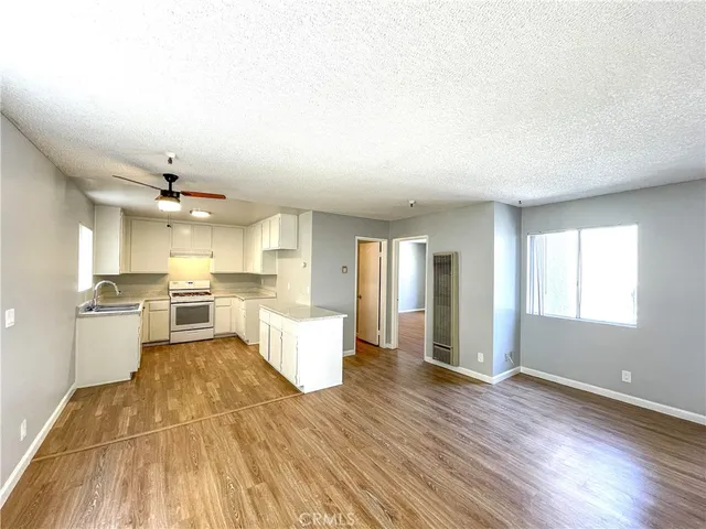a living room with stainless steel appliances kitchen island granite countertop a stove a sink dishwasher and a dining table with wooden floor