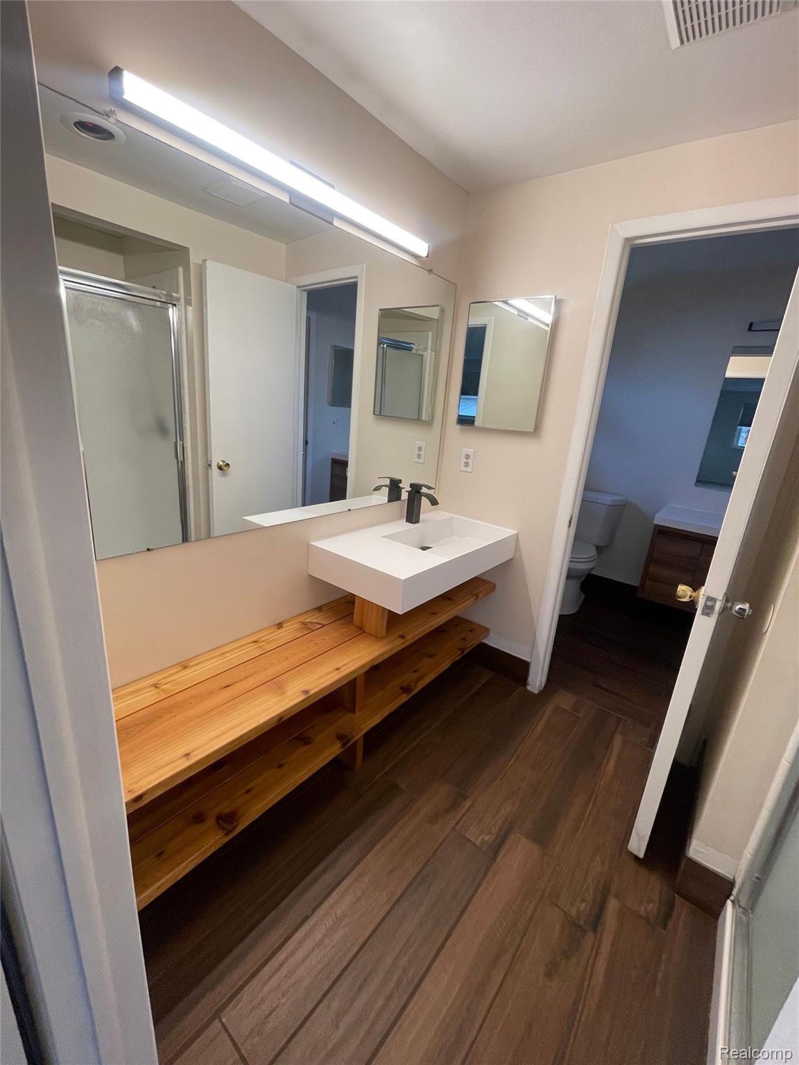 42195 Park Ridge Road Novi, MI 48375 - Photo 4 of 14 Floating vanity with a rectangular basin and matte black faucet, wood-finish flooring, full-width mirror, and built-in wood shelving
