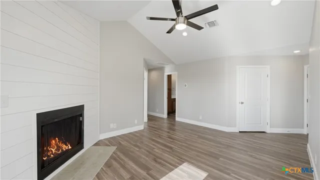 a view of an empty room with wooden floor a fireplace and a window