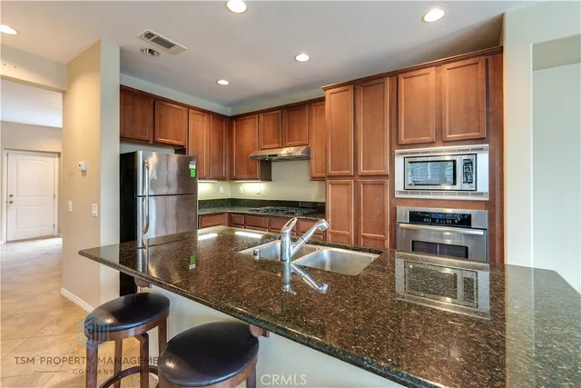 a kitchen with stainless steel appliances granite countertop a refrigerator a stove and a sink with wooden cabinets