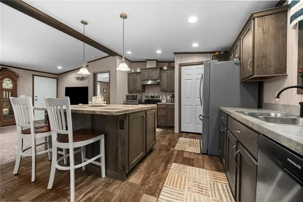 a kitchen with stainless steel appliances kitchen island granite countertop a refrigerator a sink dishwasher a stove with white cabinets and wooden floor