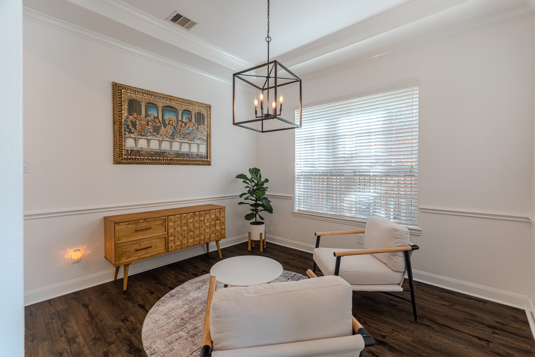 30 Fury Ranch Place The Woodlands, TX 77375 - Photo 11 of 47 This room features a cozy seating area with two modern chairs and a round table on a stylish rug. A geometric pendant light hangs above, while a wooden sideboard and wall art add character. The space is brightened by a large window, and the dark wood flooring contrasts elegantly with the white walls.