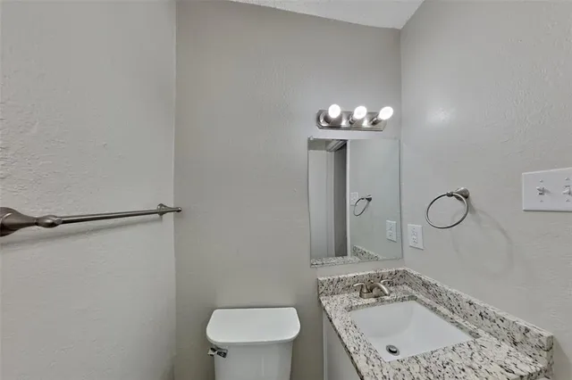 a bathroom with a granite countertop sink a toilet a mirror and shower