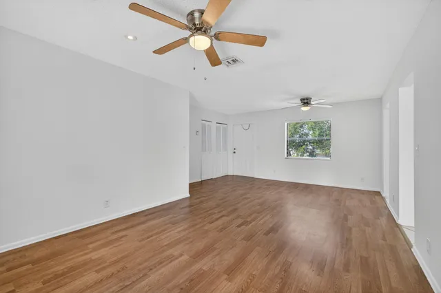 an empty room with wooden floor fan and windows