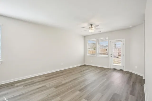 a view of an empty room with wooden floor and a ceiling fan