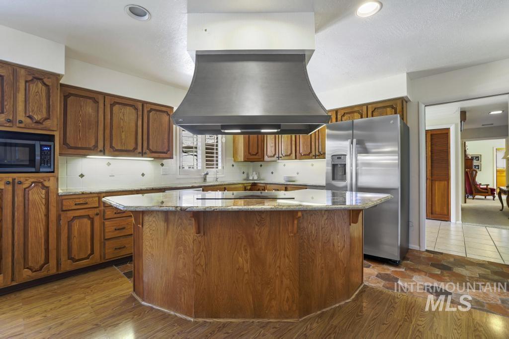 2018 Rancho Vista Drive Twin Falls, ID 83301 - Photo 15 of 50 Kitchen featuring a large central island with a built-in cooktop, a stainless steel range hood, ample wood cabinetry, light-toned countertops, and a tiled backsplash